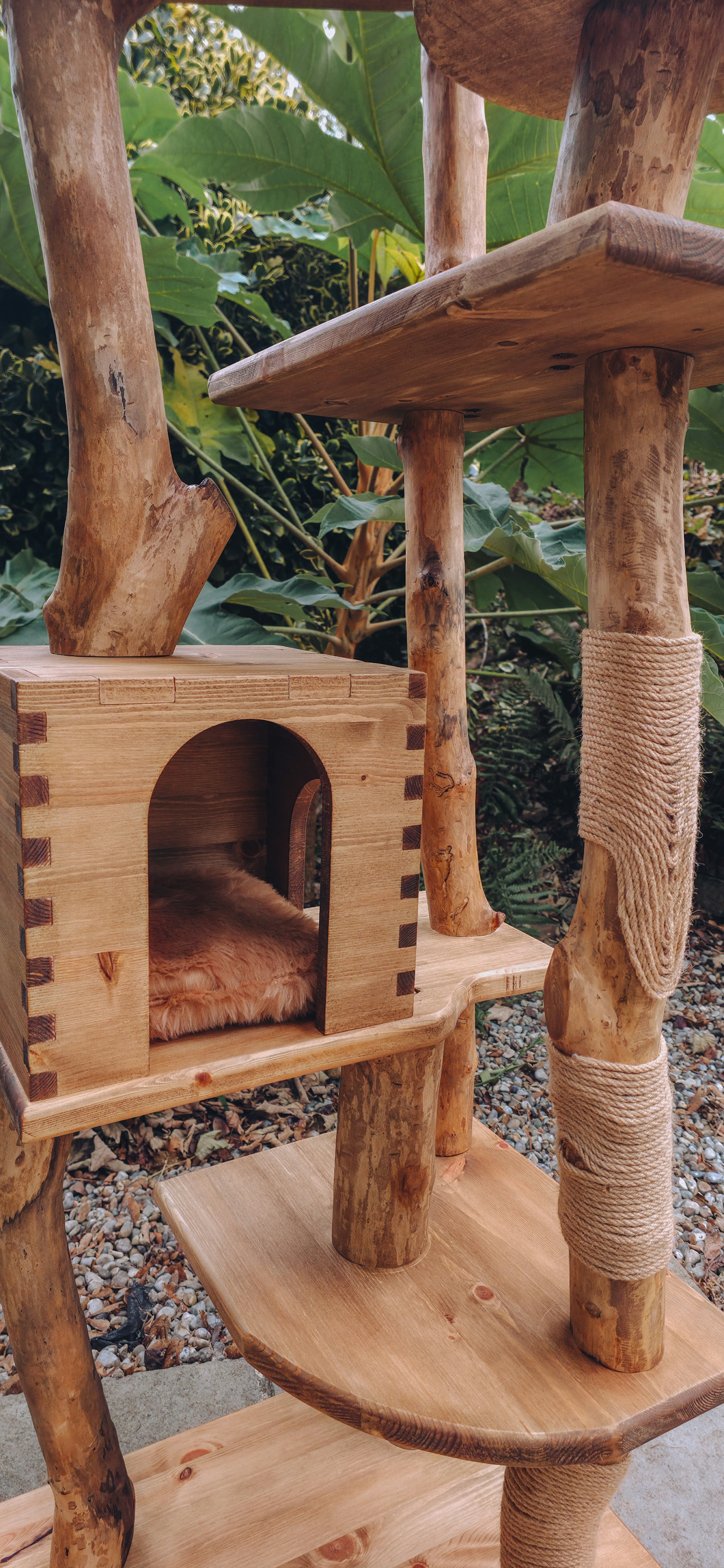 Wooden cat tree with multiple levels and a cushion, set against a natural background.