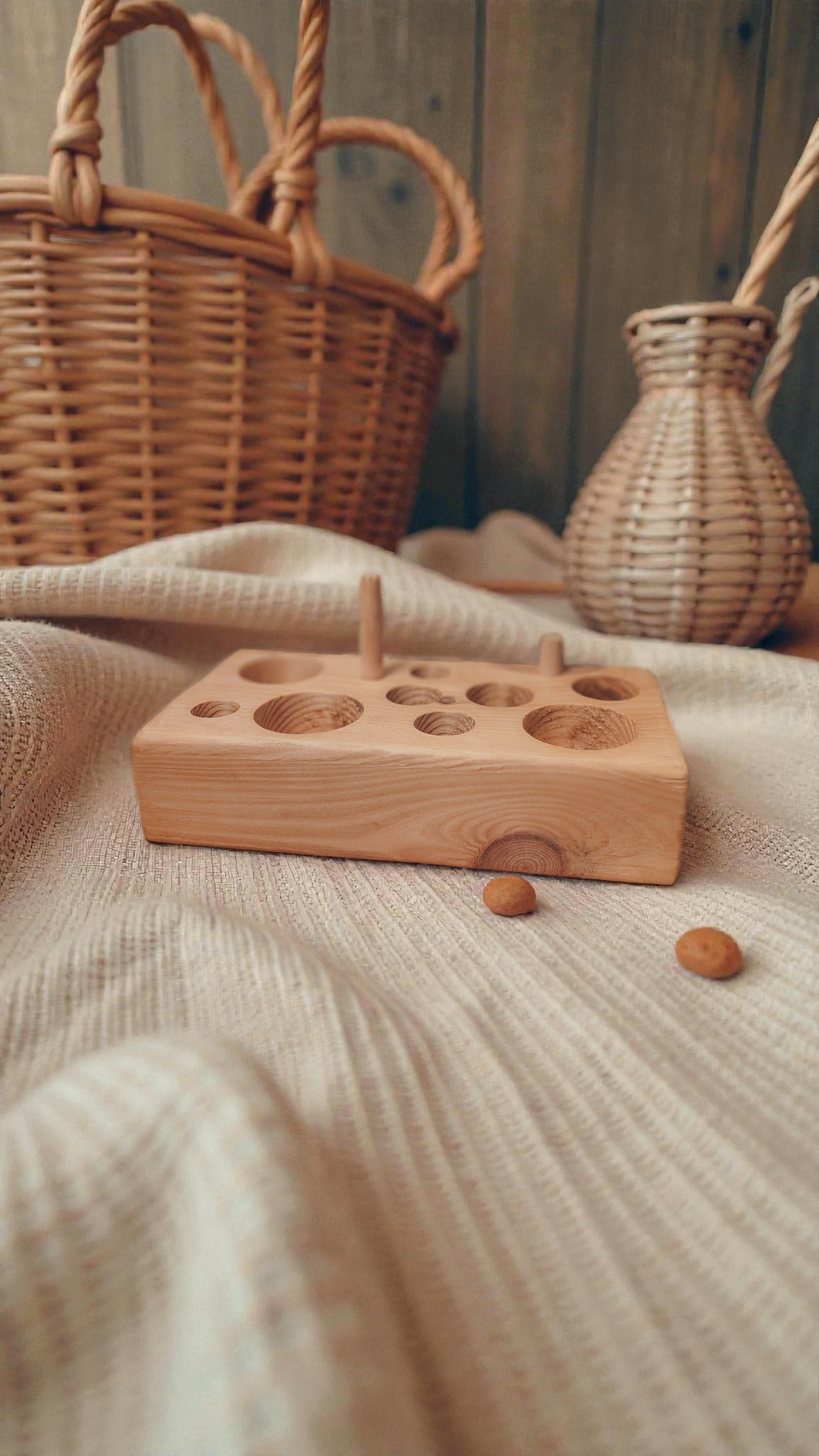 Natural wooden cat feeding puzzle toy on a linen surface with a wicker basket and vase in the background.