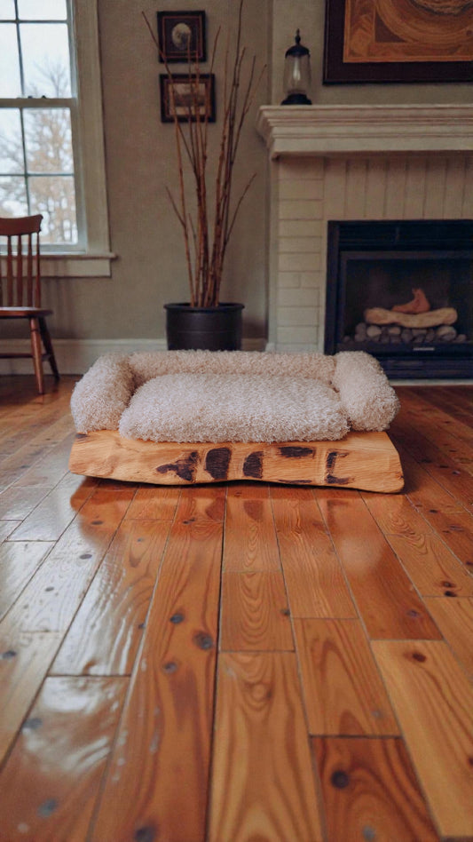 solid wood pet bed on a wooden floor in a cozy living room with a fireplace.