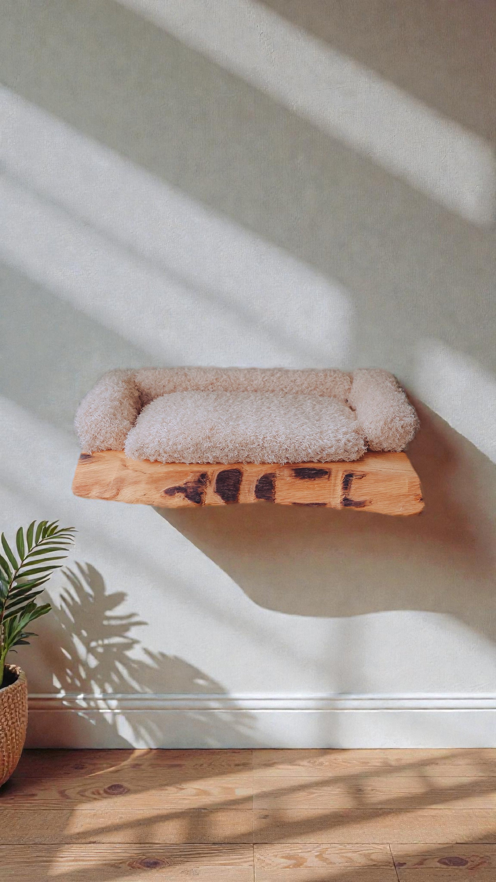Pet bed with fluffy cushion on a wooden platform in a room with sunlight casting shadows.